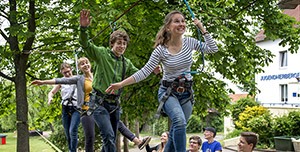 Eine Gruppe junger Leute balancieren gesichert auf einem Seil bei einer Teamübung.